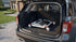 Open car trunk with a portable workbench inside, parked on a driveway.